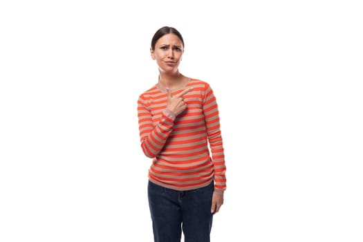 Young smart slim brunette woman dressed in a striped orange blouse and jeans points with her hands to the advertising space.