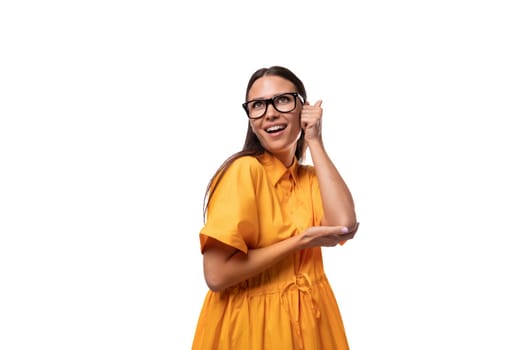 Caucasian young slender woman with black straight hair with glasses and in a yellow dress is flirting and shy.