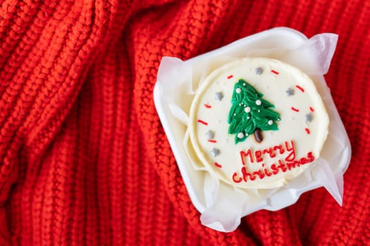 Holiday concept. Christmas cake with the inscription Merry Christmas , decorated with icing, on a red warm background, top view