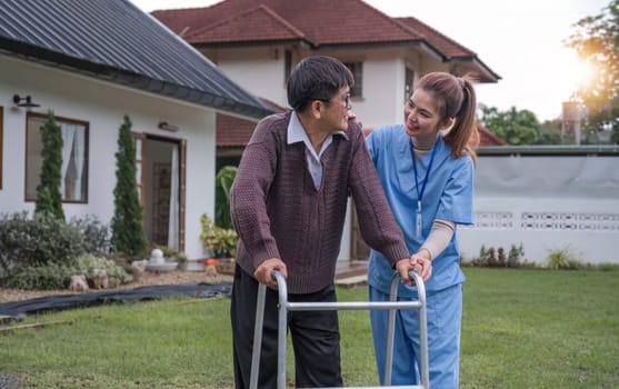 Asian woman caregiver helping senior man walking. Nurse assisting he old man patient at nursing home. Senior man using walker being helped by nurse at home. Elderly patient care and health lifestyle.