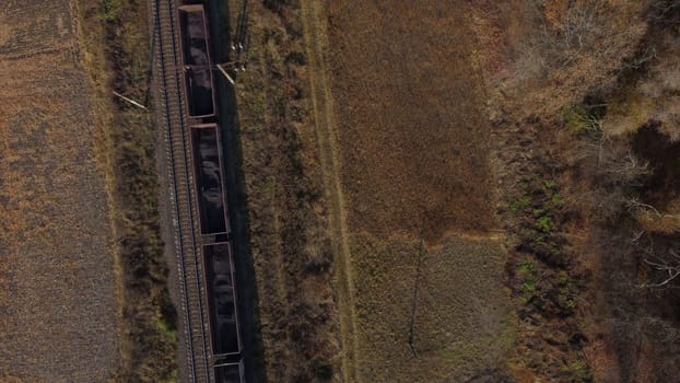 Aerial drone view flight over movement of train with carriages filled coal an autumn day. Top view Transportation and Rail freight. Freight cars or railway wagon rides on railroad. Delivery of cargo