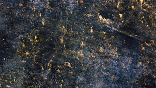 Aerial drone view flight over black ash of field of burned brown yellow dry grass and white smoke on sunny autumn day. View from above. Texture natural background of ecological environmental disaster.