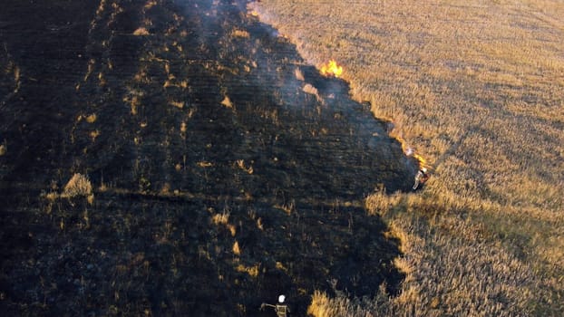 Aerial view Fire extinguishing. Fireman extinguishing burning dry grass. Open flames of fire and smoke. Yellow dry grass and black ash from burnt plants.Ecological catastrophy. Fire on field in steppe