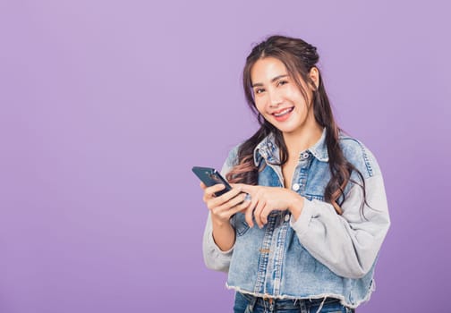 Portrait of Asian beautiful young woman confident wear denim jeans shirt hold smartphone typing smartphone, Happy lifestyle female write message look phone, studio shot isolated on purple background