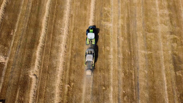 Hay bale tractor. Tractor harvesting hay into bales in field on sunny day. Aerial drone view. Tractor drives across field and makes bales from cut straw. Field and agricultural work, baler. Ukraine