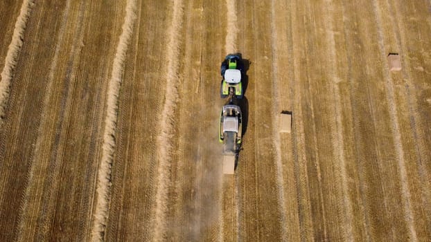 Hay bale tractor. Tractor harvesting hay into bales in field on sunny day. Aerial drone view. Tractor drives across field and makes bales from cut straw. Field and agricultural work, baler. Ukraine