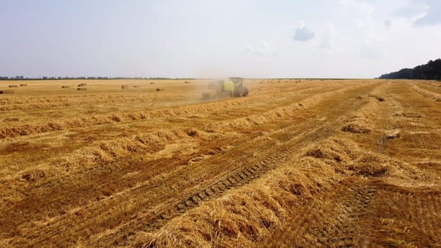 Hay bale tractor. Tractor harvesting hay into bales in field on sunny day. Aerial drone view. Tractor drives across field and makes bales from cut straw. Field and agricultural work, baler. Ukraine