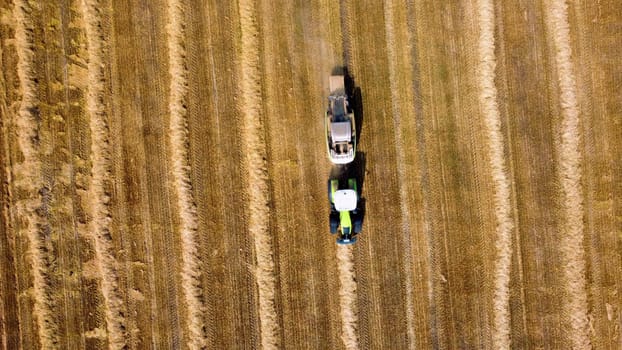 Hay bale tractor. Tractor harvesting hay into bales in field on sunny day. Aerial drone view. Tractor drives across field and makes bales from cut straw. Field and agricultural work, baler. Ukraine