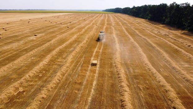 Hay bale tractor. Tractor harvesting hay into bales in field on sunny day. Aerial drone view. Tractor drives across field and makes bales from cut straw. Field and agricultural work, baler. Ukraine