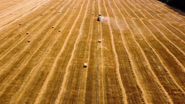 Hay bale tractor. Tractor harvesting hay into bales in field on sunny day. Aerial drone view. Tractor drives across field and makes bales from cut straw. Field and agricultural work, baler. Ukraine