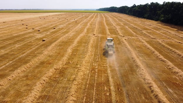 Hay bale tractor. Tractor harvesting hay into bales in field on sunny day. Aerial drone view. Tractor drives across field and makes bales from cut straw. Field and agricultural work, baler. Ukraine