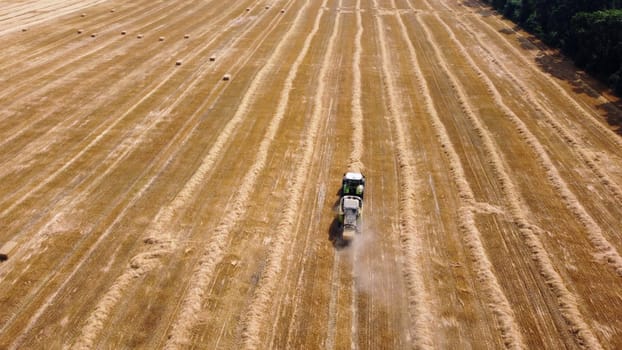 Hay bale tractor. Tractor harvesting hay into bales in field on sunny day. Aerial drone view. Tractor drives across field and makes bales from cut straw. Field and agricultural work, baler. Ukraine