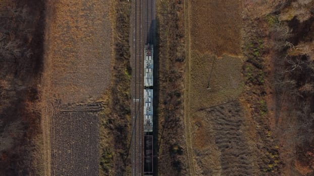 Aerial drone view flight over movement of train with carriages filled coal an autumn day. Top view Transportation and Rail freight. Freight cars or railway wagon rides on railroad. Delivery of cargo