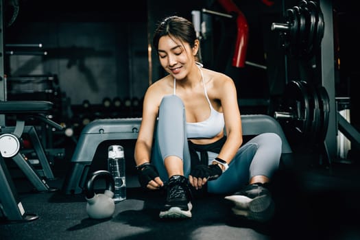 Woman tying the shoelace of her running shoe, holding a shaker bottle of water. The shot emphasizes the importance of staying hydrated during exercise.