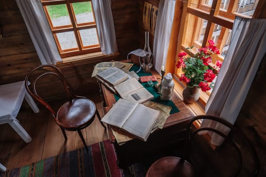 Open books are lying on a desk in a rustic study room illuminated by natural light from a window with red flowers