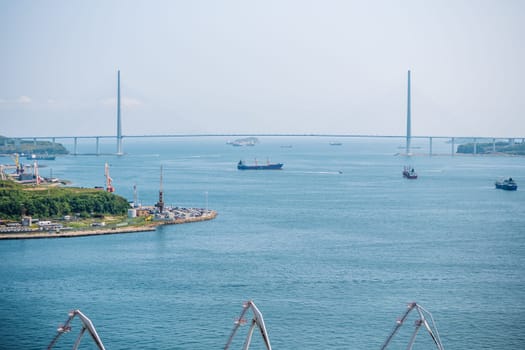 Cargo vessels navigating beneath russian bridge, spanning waterway on clear day, connecting distant landmasses with maritime transport
