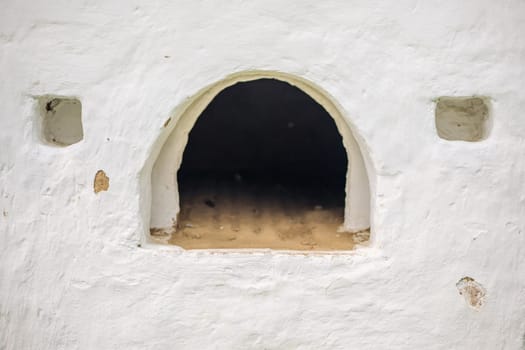 Whitewashed facade of a traditional russian stove featuring a large arch and two small square openings, showcasing historical cooking methods