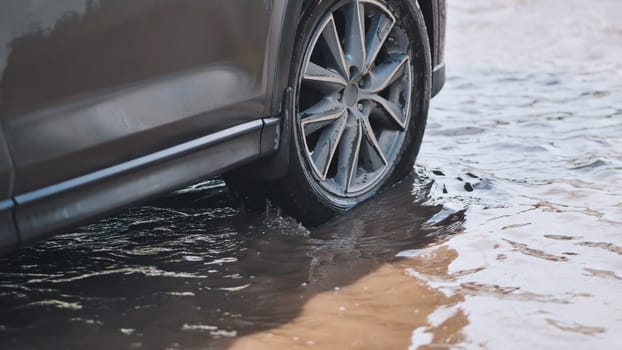 Close up of car wheel driving through flooded road during natural disaster, heavy rain and flood