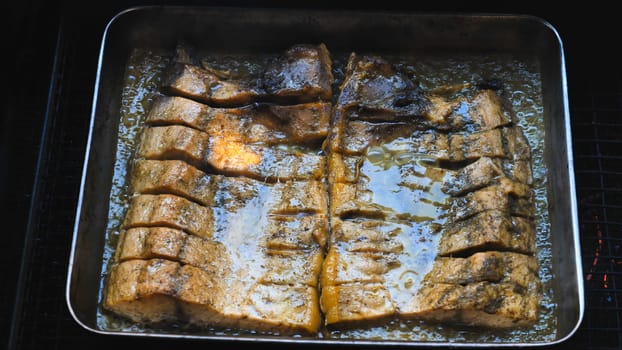 Scored smoked fish fillets roasting golden brown in metal pan, releasing rich, caramelizing juices during slow cooking process