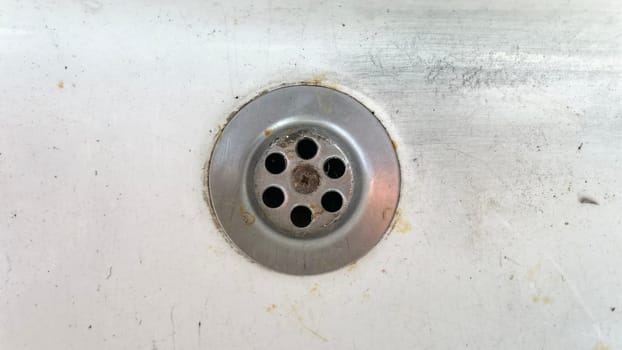 A close view of a kitchen sink's drain showing rust and dirt buildup around the opening.