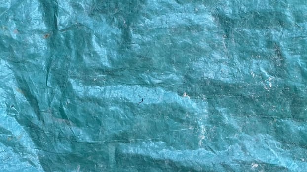 A close-up view of a textured blue tarp with visible creases and color variations under natural light.