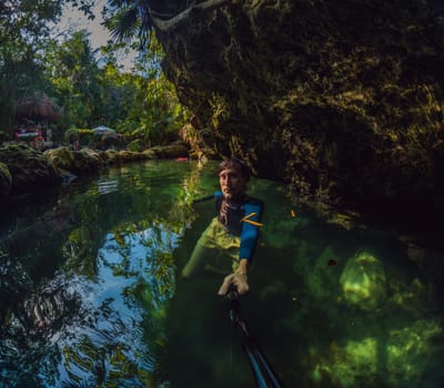Man tourist in the water of a Mexican cenote surrounded by natural beauty. Adventure travel, eco-tourism, and exploration concept in a tropical paradise.
