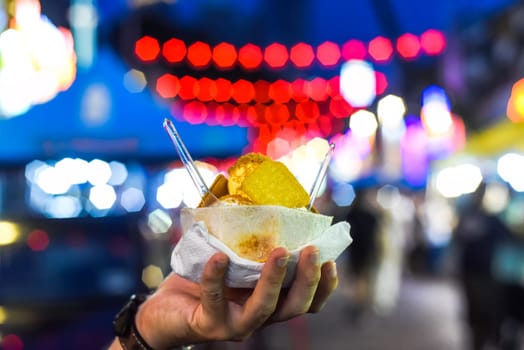 Hand holding coconut and mango ice cream in coconut shell against lights of Jalan Alor street food market in Kuala Lumpur