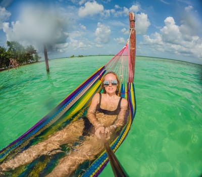 Woman tourist relaxing on a hammock above the turquoise waters of Lake Bacalar, Mexico. Peaceful retreat, tropical paradise, and relaxation concept in a serene natural setting.