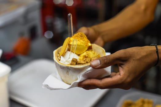 Hand holding coconut and mango ice cream in coconut shell in Jalan Alor street food market in Kuala Lumpur