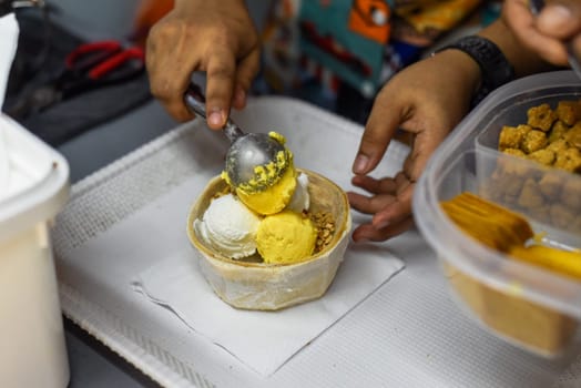 Hand holding coconut and mango ice cream in coconut shell in Jalan Alor street food market in Kuala Lumpur