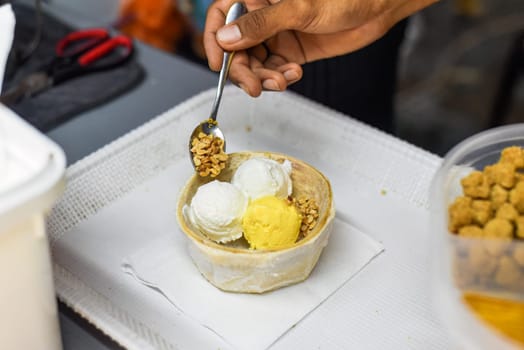 Hand holding coconut and mango ice cream in coconut shell in Jalan Alor street food market in Kuala Lumpur