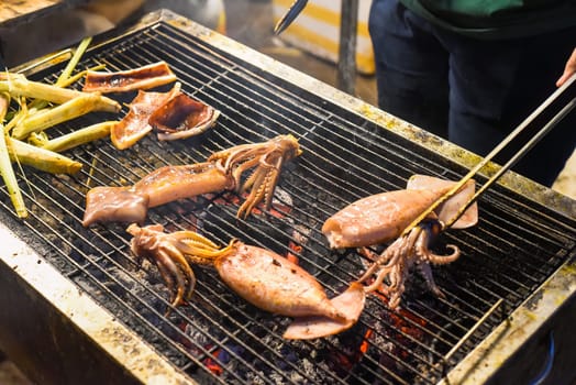 Many squids on a grill in vietnamese night market in food festival, process of cooking