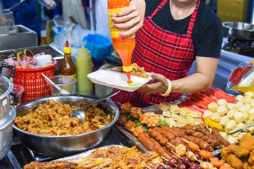 Vietnamese woman serving chicken paws in plastic box with chili in vietnamese night market