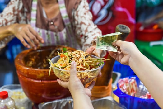 Vietnamese woman serving noodles with vegetables in vietnamese night market in food festival, person buying
