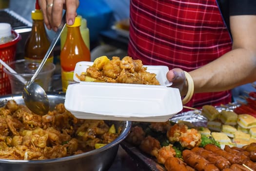 Vietnamese woman serving chicken paws in plastic box with chili in vietnamese night market
