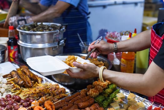 Vietnamese woman serving chicken paws in plastic box with chili in vietnamese night market