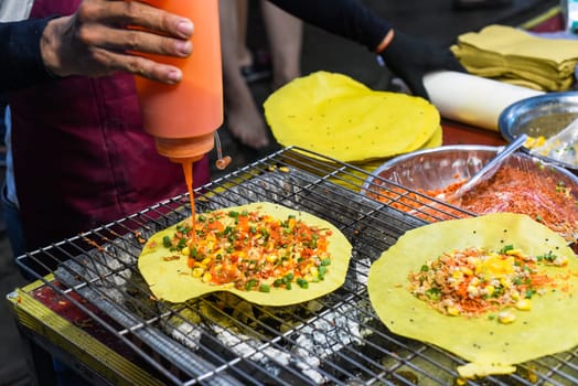 Grilled vietnamese pancake with eggs, sausages and sauces in vietnamese night market in food festival