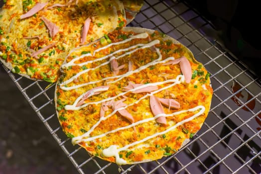 Grilled vietnamese pizza with eggs, sausages and sauces in vietnamese night market in Da Lat