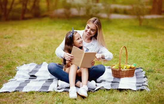 Mother And Daughter Reading Book Enjoying Time Together During Summer Picnic In Park Outside. Free Space For Text