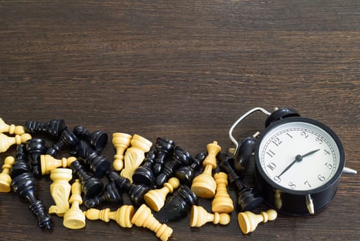 Chess pieces and alarm clock on wooden background. Business metaphor. Copy space