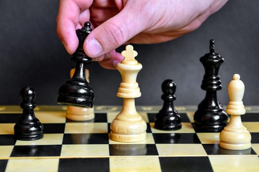 Male hand holding the black queen to defeat the white king on a chessboard on black background. Checkmate