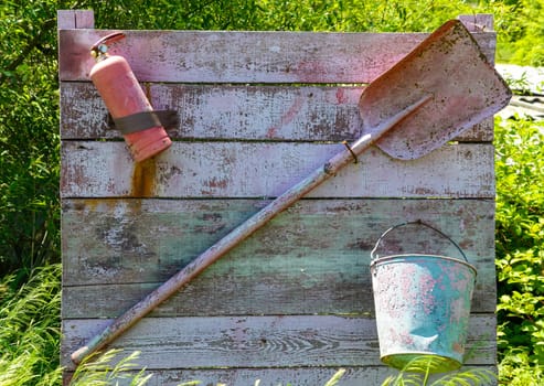 Fire extinguisher, bucket and shovel hanging on the board. Shabby and old