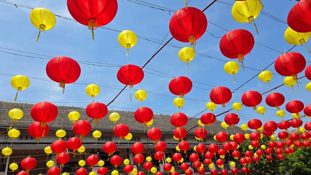 Vibrant red and yellow lanterns suspended across open balconies under a serene blue sky, representing festive celebrations of chinese new year and traditional cultural decor. good for background