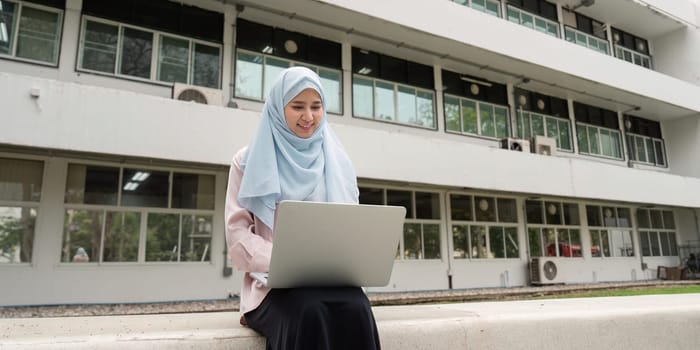A focused Muslim businesswoman in a hijab diligently working on her laptop, enjoying a serene outdoor environment.