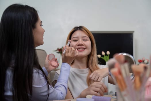 A beauty broker applying blush on a friend cheeks during a live broadcast, sharing beauty tips and enjoying a joyful moment together.