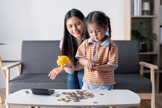 A mother and her daughter joyfully count coins on a table, engaging in a fun lesson about saving money in their stylish living room.