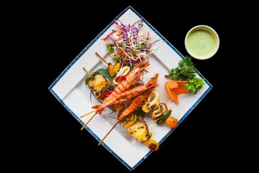 Grilled shrimps with fish on skewers on isolated on black background top view