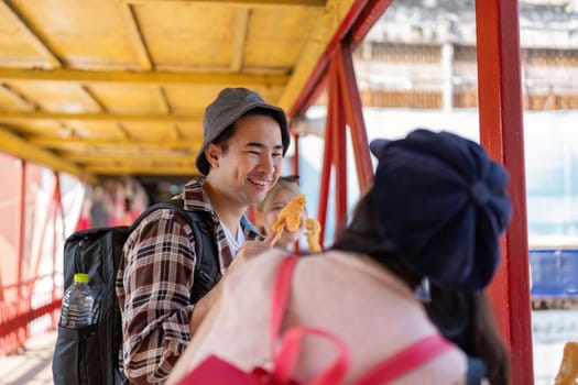 A smiling Asian man shares a joyful moment with friends while enjoying street food on a colorful bridge in a lively city.