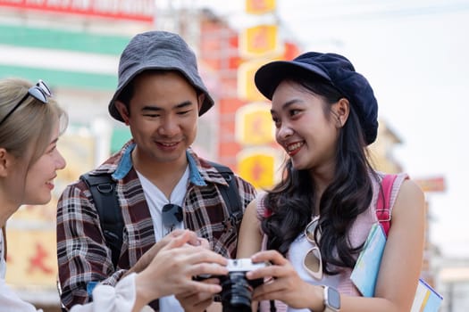 A group of young Asian friends excitedly looking at photos on a camera, capturing memories together in a lively market, highlighting the joy of travel and friendship.