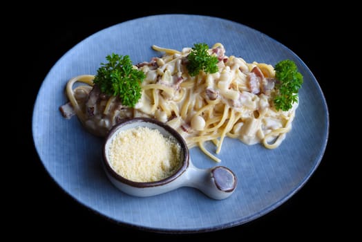 Pasta carbonara with bacon on blue plate isolated on black background top view